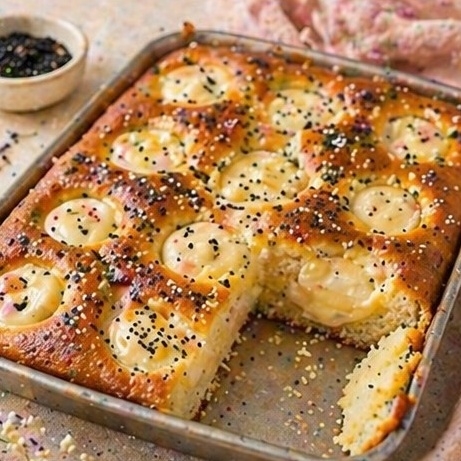 Goldbrauner Hefekuchen vom Blech mit großen hellen Creme-Mulden sowie hellen und dunklen Saaten
